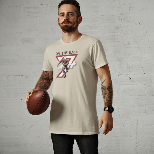 Man wearing beige hand-drawn rugby sports tee holding rugby ball with comic-style illustration and text "On The Ball"
