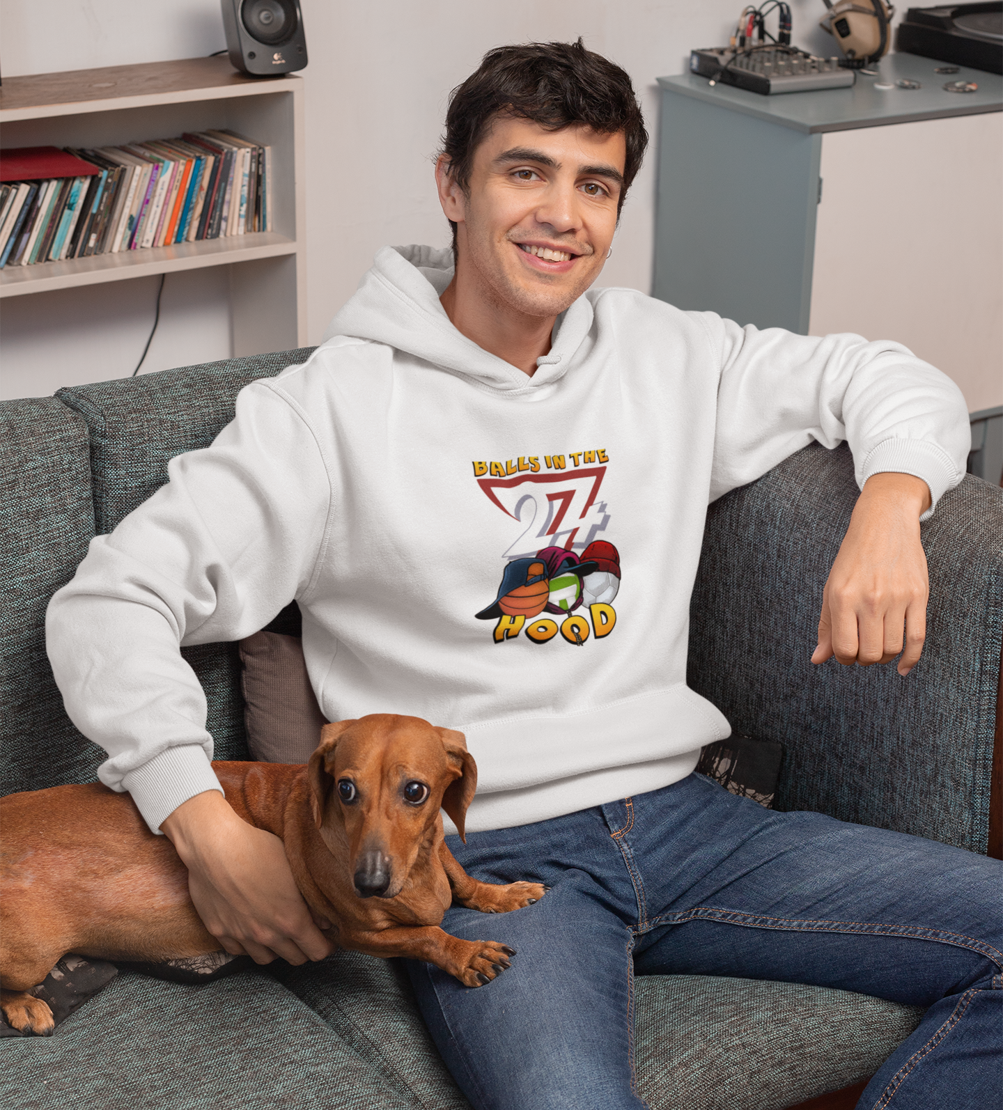 Man wearing white printed hoodie sitting on couch with a dog in a cozy room