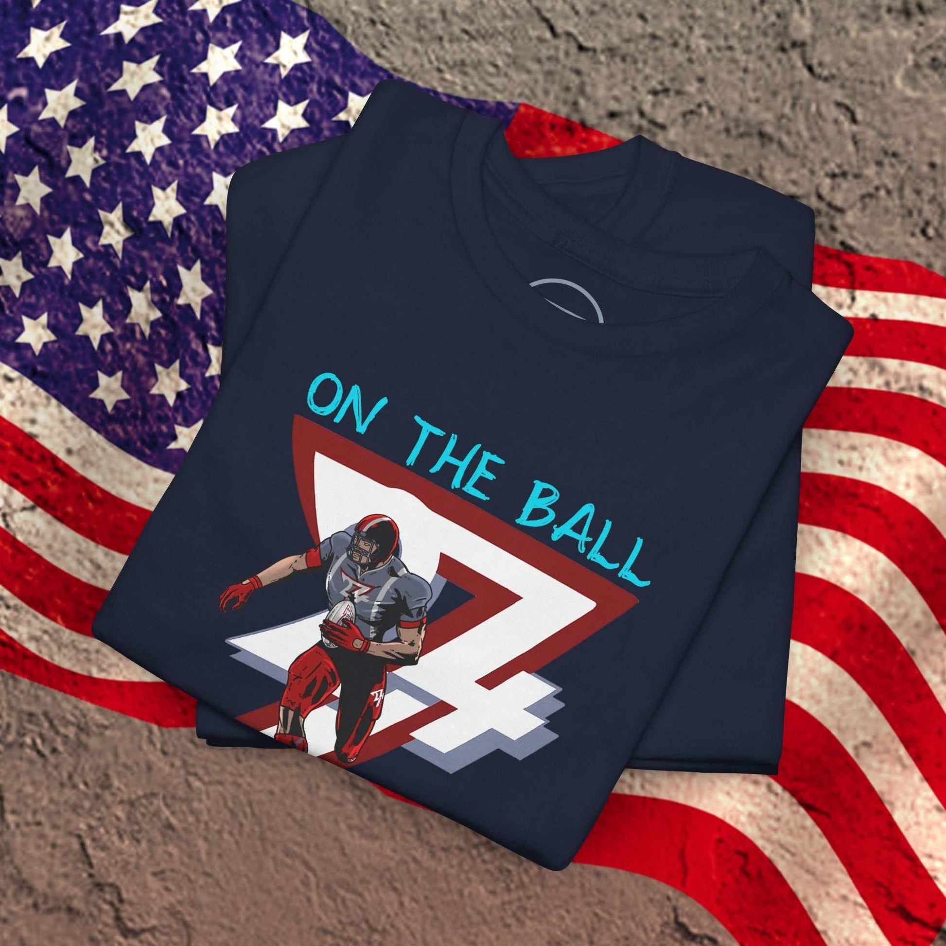 Navy American football tee with hand-drawn comic-style player graphic and "On The Ball" text on chest, laid on American flag background