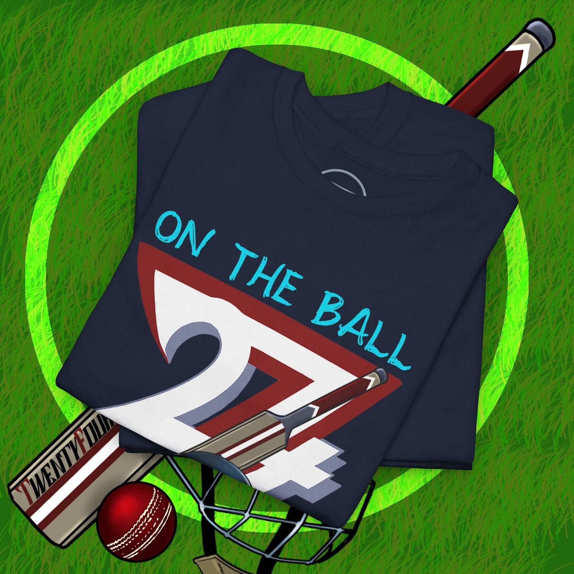Navy blue cricket tee with hand-drawn 90s style "On The Ball 24/7" graphic, cricket bat, ball, and helmet on grass background