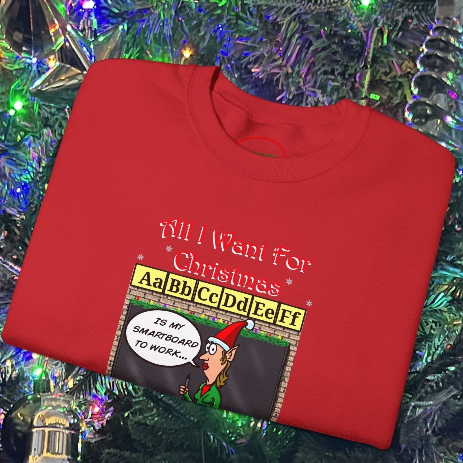 Red Teacher Christmas Sweatshirt with funny cartoon teacher and "All I Want For Christmas is my Smartboard to Work" text, folded on Christmas tree background