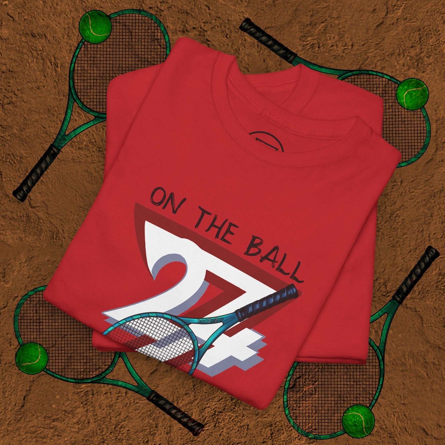 Red tennis tee with "On the Ball 24/7" hand-drawn graphic on folded shirt surrounded by tennis rackets and balls