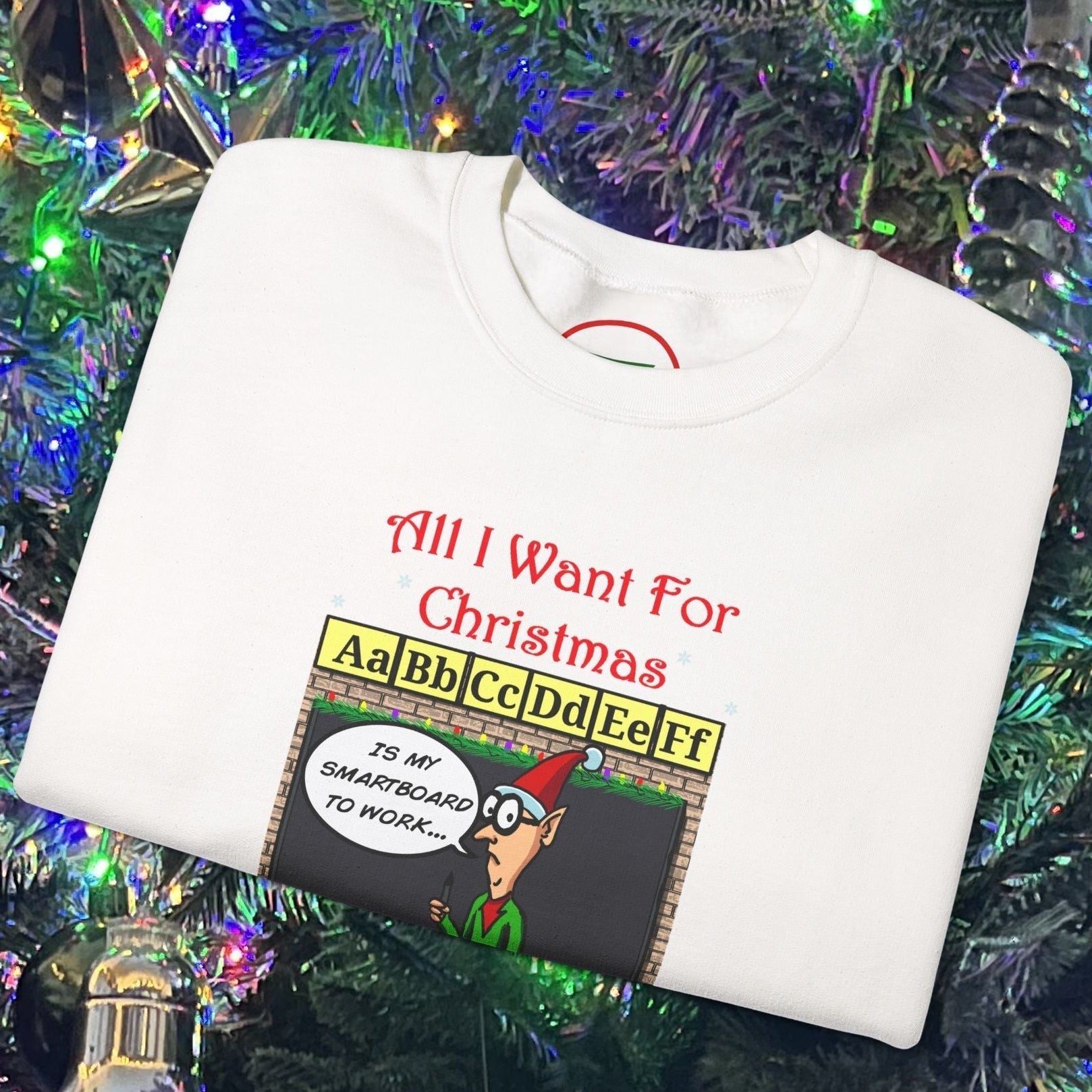 White Funny Cartoon Teacher Christmas sweatshirt with comic design and holiday theme, folded on Christmas tree background