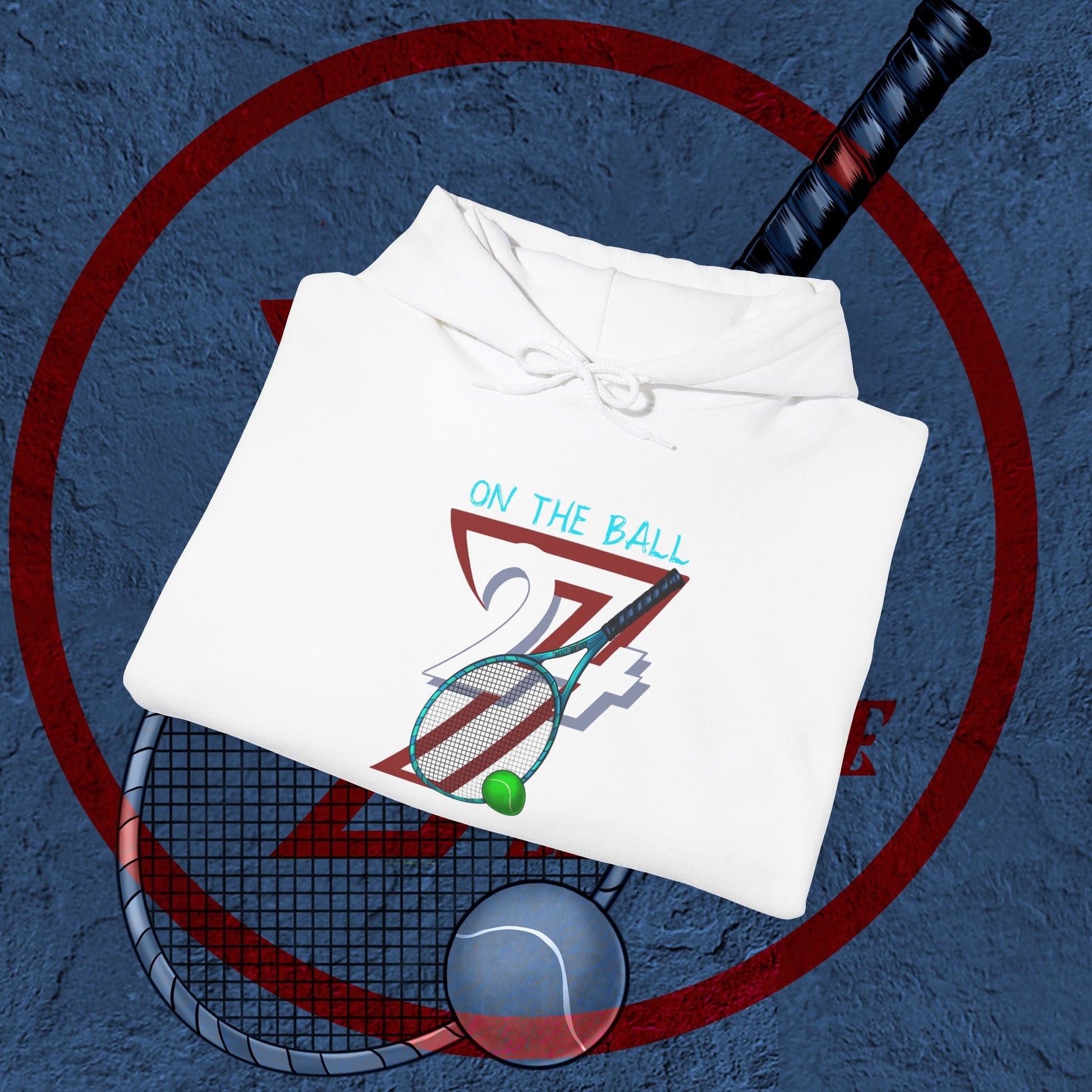White tennis hoodie with hand-drawn tennis racket, ball, and "On The Ball 24/7" design, folded on a textured blue surface with tennis elements in background