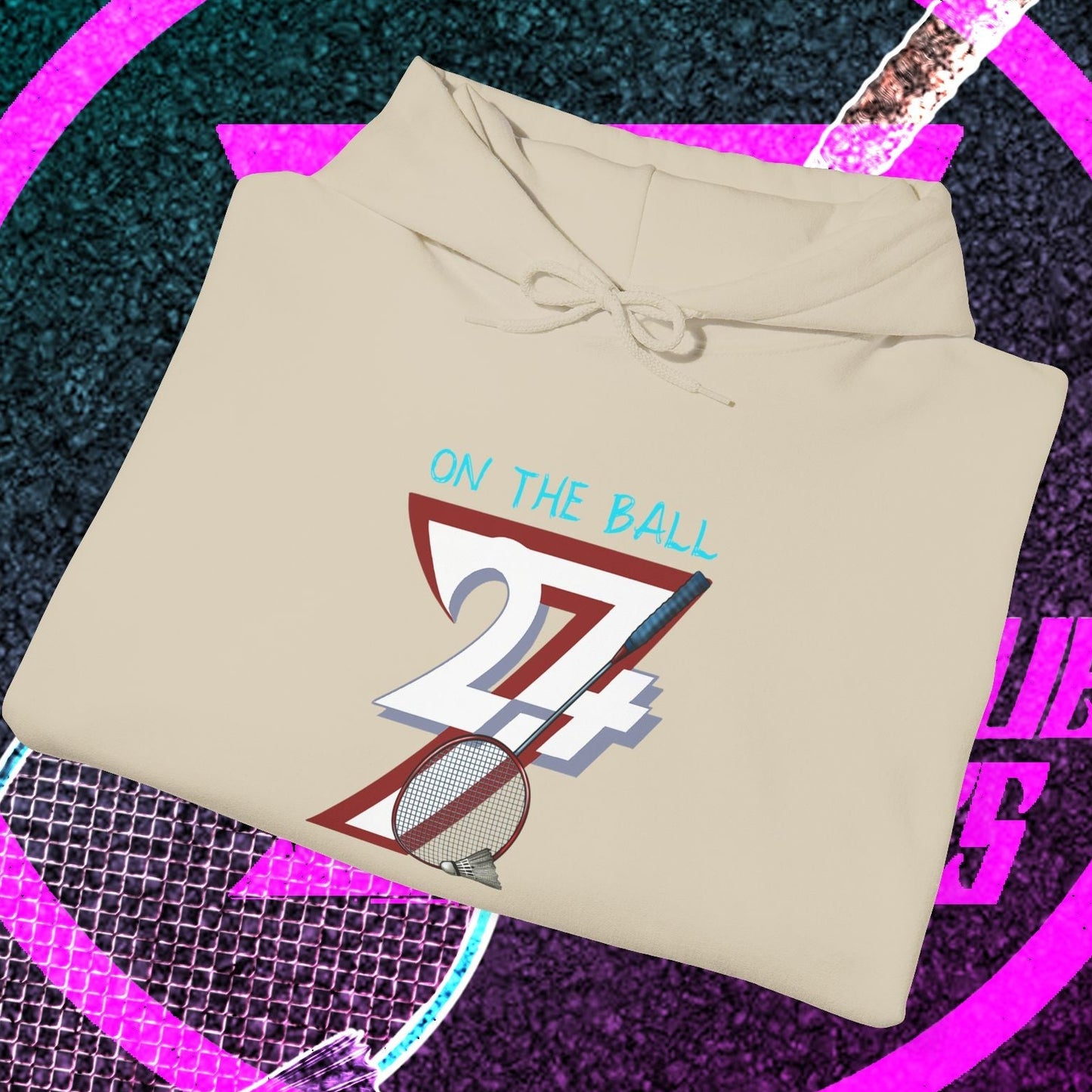 beige badminton hoodie sweatshirt with "On The Ball 24/7" design folded on black and purple sports background