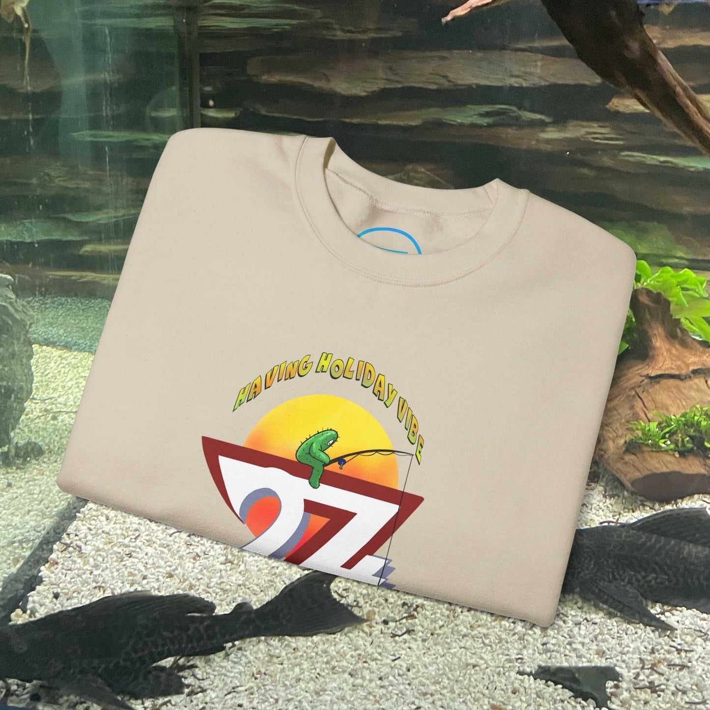 beige fishing cactus sweatshirt with funny cartoon design folded on gravel surface with mossy rocks and plants background