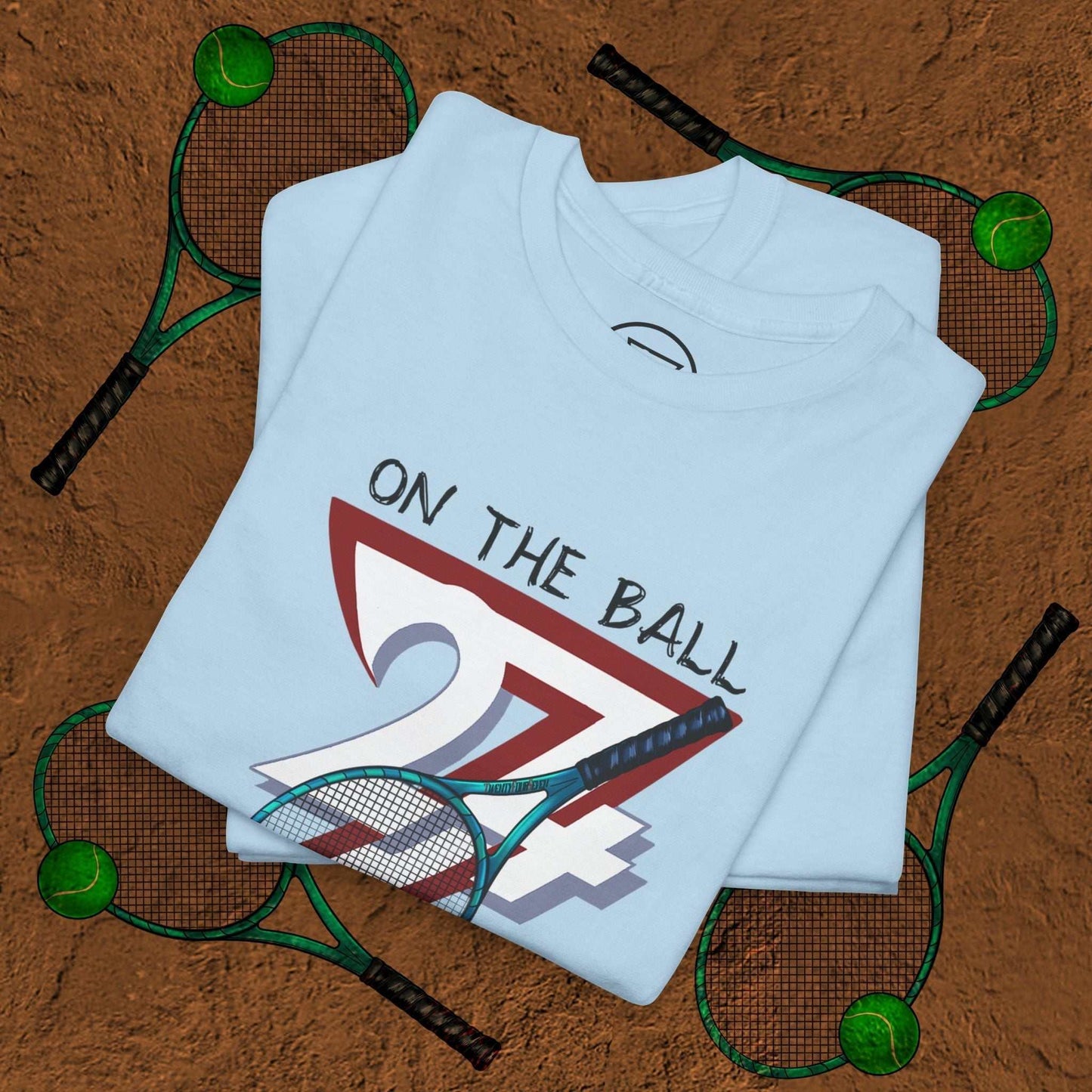 blue tennis tee with "On the Ball 24/7" hand-drawn tennis design and racquets on clay court background