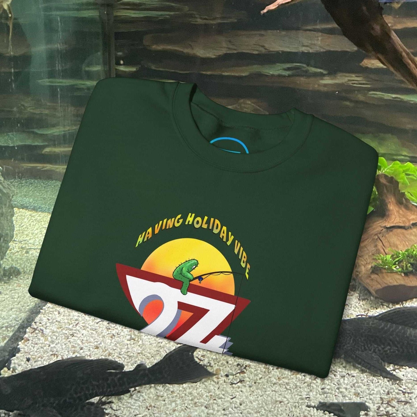 dark green fishing cactus sweatshirt with cartoon fishing design and "Having Holiday Vibe" text folded on a surface