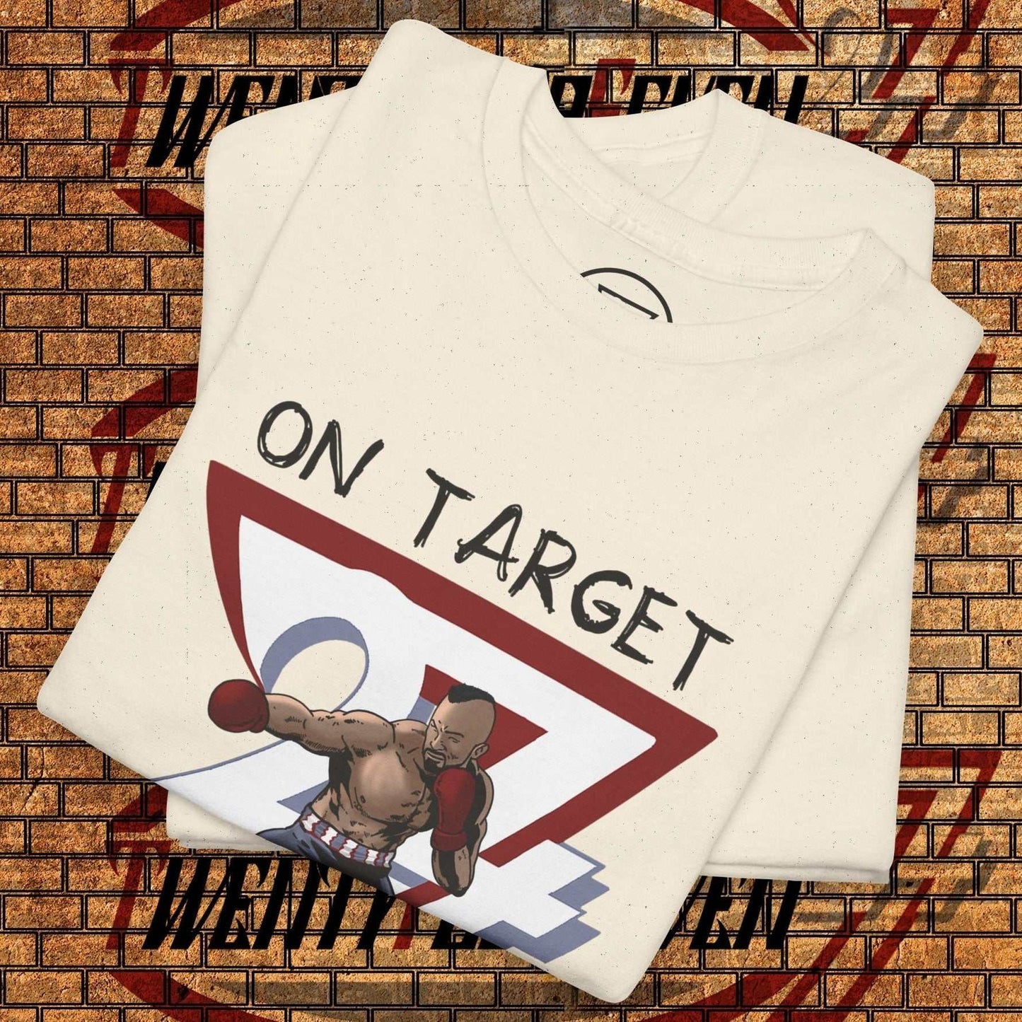 folded boxing graphic shirt with hand-drawn boxer illustration and "ON TARGET" text on cream fabric against brick wall background