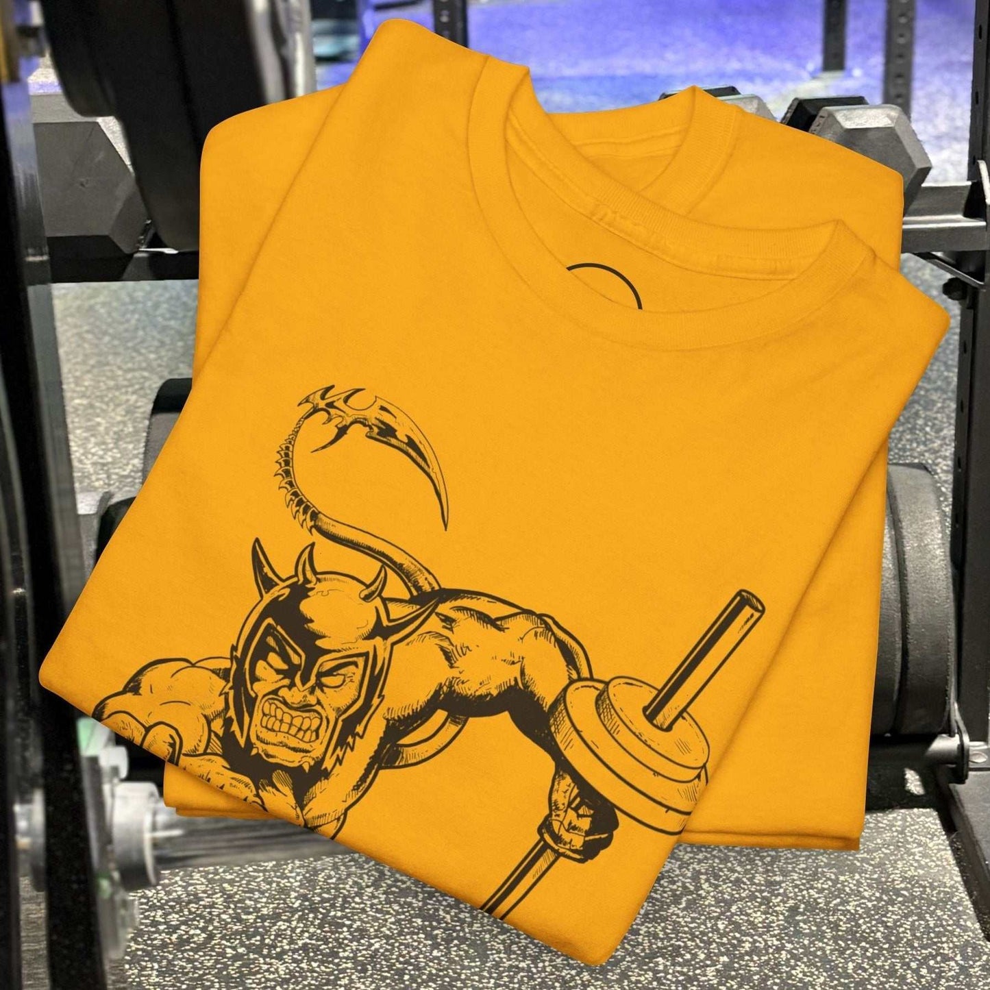 folded yellow hand-drawn comic-style gym tee with muscular devil illustration holding barbell on gym floor