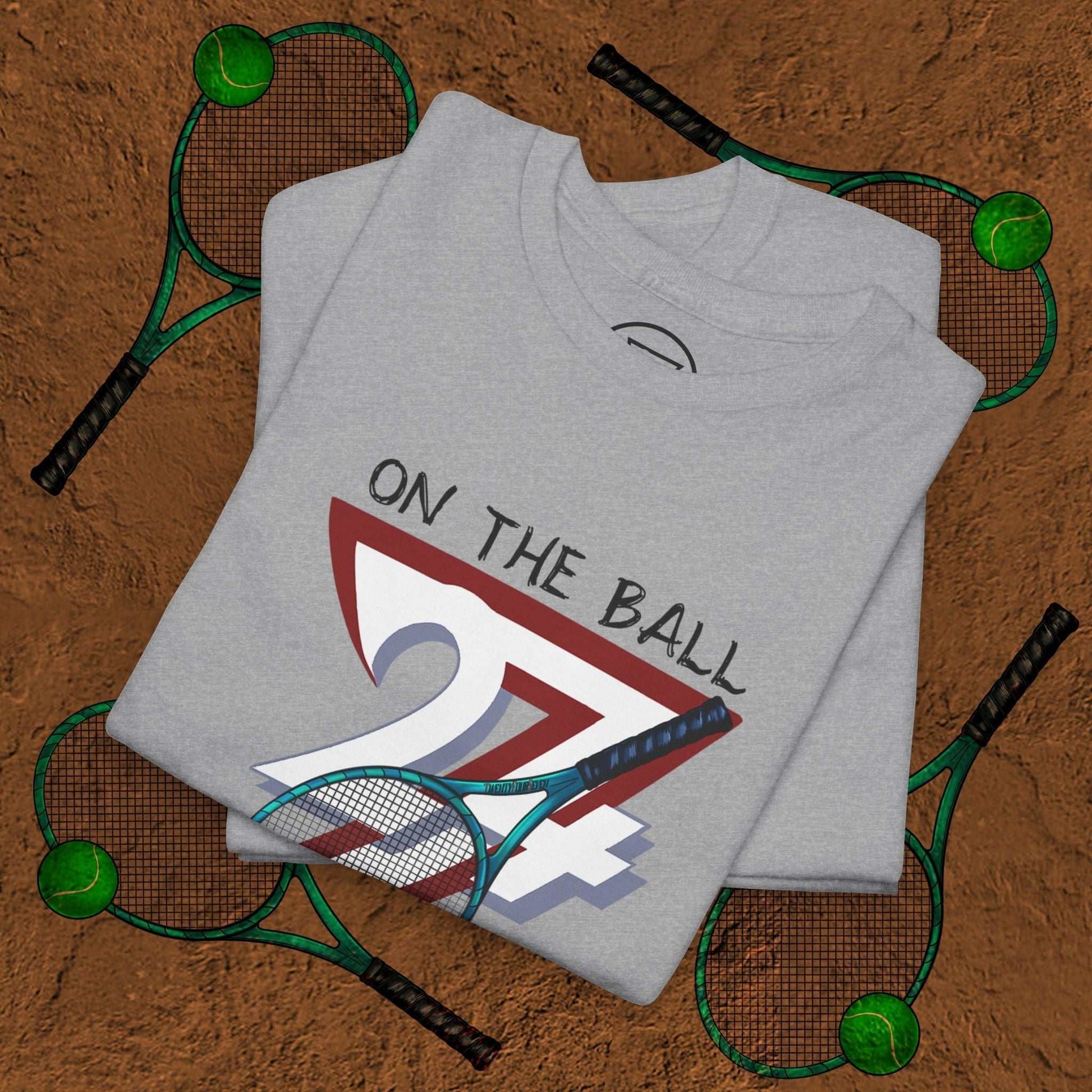 grey tennis tee with hand-drawn "On the Ball 24/7" graphic and tennis racket design on brown background with tennis balls and rackets