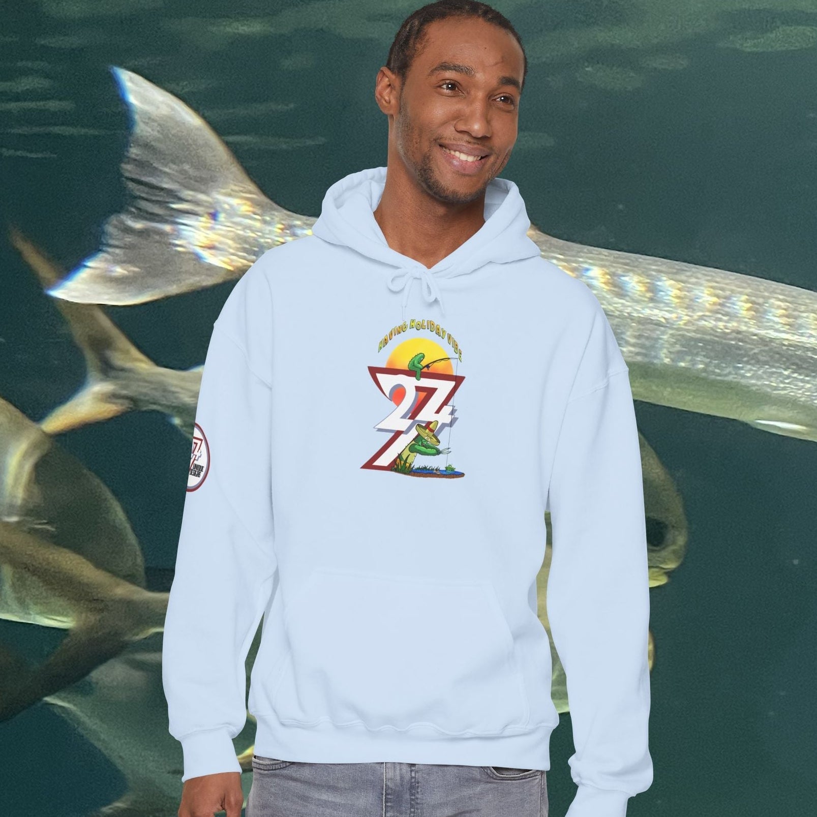 man wearing light blue funny fishing hoodie with cactus design standing in front of large fish aquarium