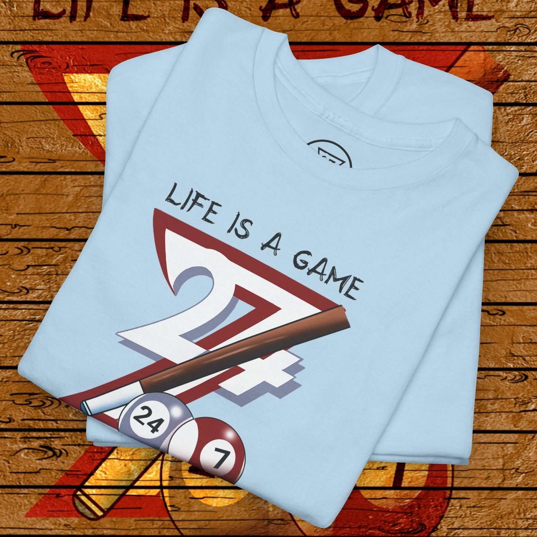 light blue pool tee with "Life is a Game" text and billiards balls and cue design folded on wooden background