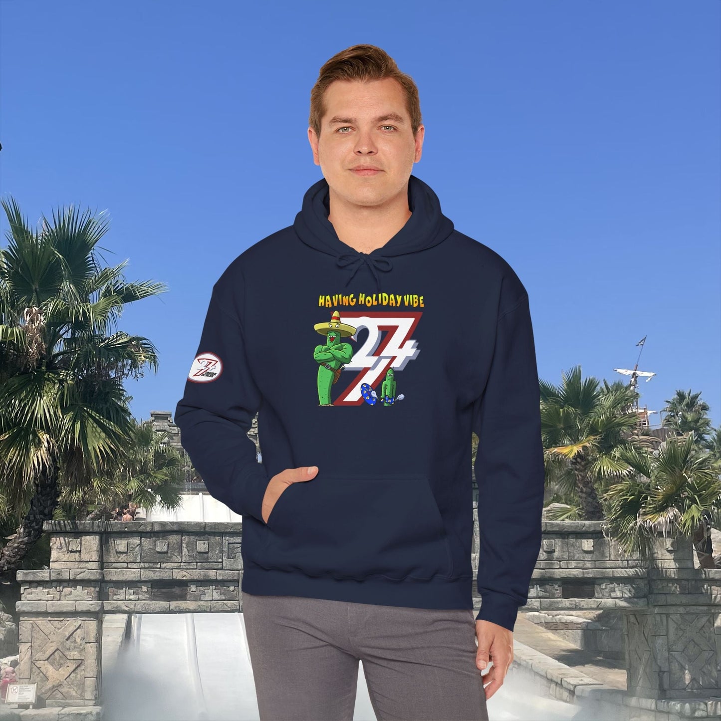 man wearing navy cactus hoodie with cartoon holiday design and kangaroo pocket outdoors on sunny day
