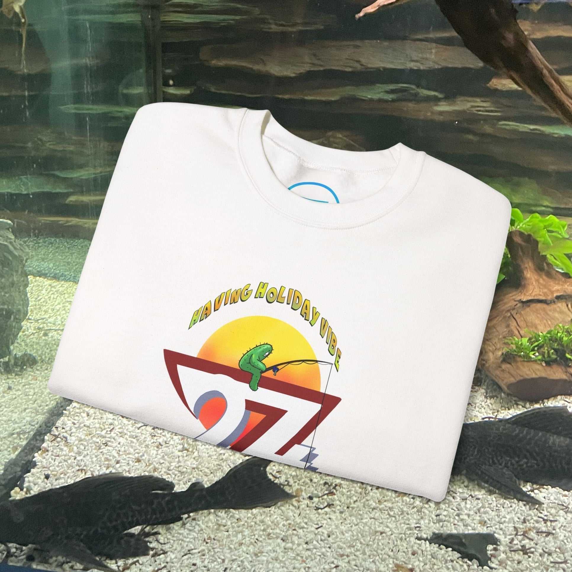 white fishing cactus sweatshirt with colorful cartoon fishing design and "Fishing Holiday Vibes" text folded on aquarium background